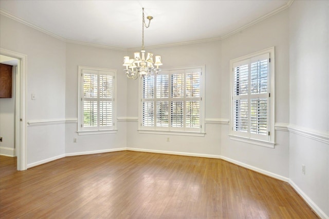 empty room featuring plenty of natural light, wood-type flooring, crown molding, and a chandelier