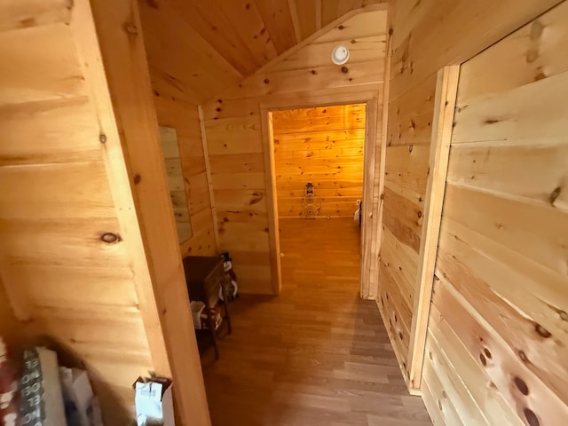 hall with light hardwood / wood-style floors, vaulted ceiling, and wooden walls