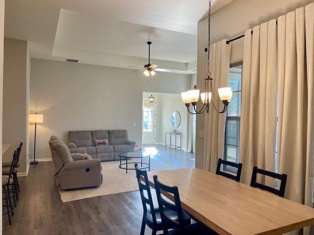 dining room with ceiling fan with notable chandelier, a raised ceiling, and dark wood-type flooring