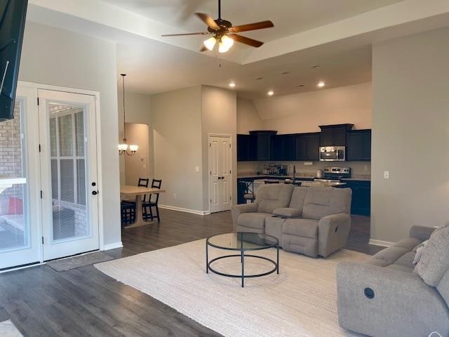 living room with ceiling fan with notable chandelier, dark hardwood / wood-style flooring, and vaulted ceiling