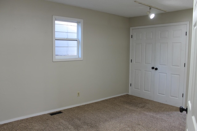 unfurnished bedroom featuring carpet floors, a closet, and rail lighting