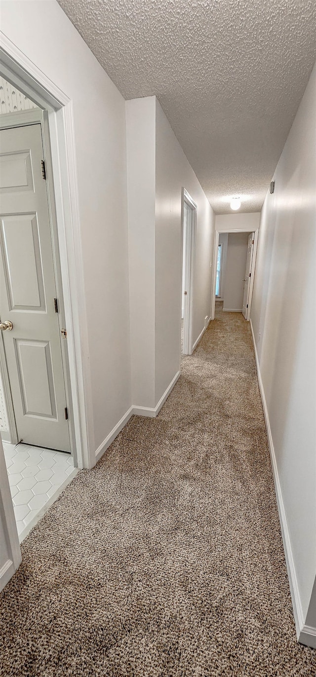 hall with light colored carpet and a textured ceiling