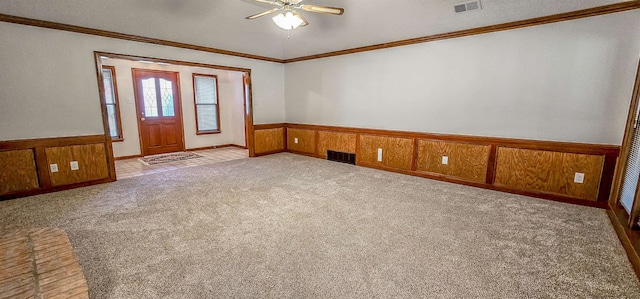 carpeted spare room featuring ceiling fan, crown molding, and wood walls