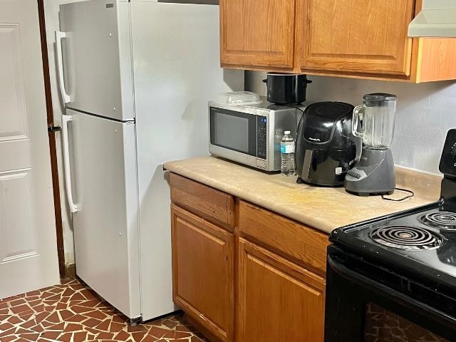 kitchen with white fridge, custom exhaust hood, black electric range oven, and dark tile patterned flooring