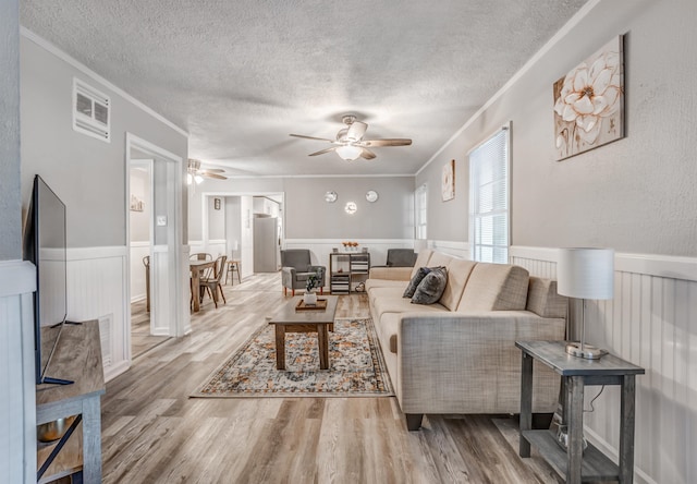 living room featuring a textured ceiling, ceiling fan, light wood-type flooring, and ornamental molding