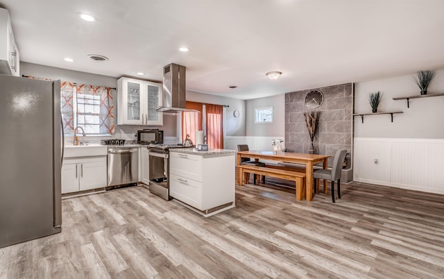 kitchen with white cabinets, wall chimney exhaust hood, stainless steel appliances, and light wood-type flooring