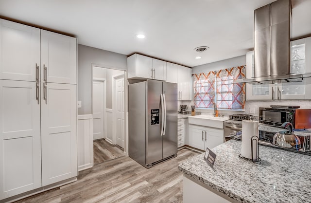 kitchen featuring island exhaust hood, appliances with stainless steel finishes, light stone counters, light hardwood / wood-style flooring, and white cabinets