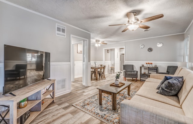 living room with ceiling fan, light hardwood / wood-style floors, crown molding, and a textured ceiling