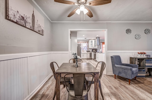 dining space featuring a textured ceiling, ceiling fan, light wood-type flooring, and crown molding