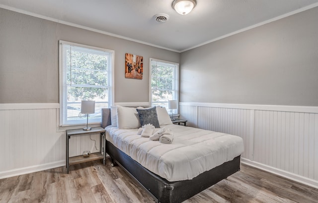 bedroom with multiple windows, wood-type flooring, and ornamental molding