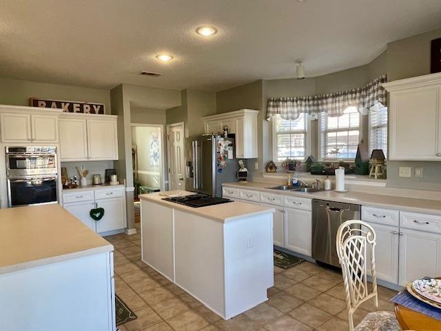 kitchen with appliances with stainless steel finishes, a center island, white cabinetry, and sink