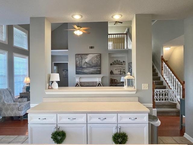 interior space featuring white cabinetry, ceiling fan, light hardwood / wood-style flooring, a towering ceiling, and a textured ceiling