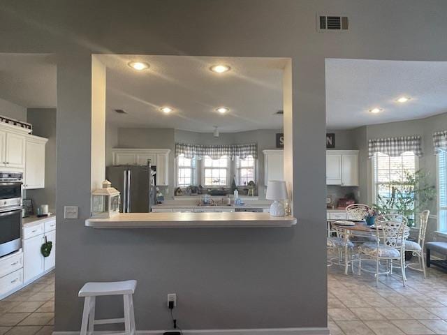 kitchen with kitchen peninsula, a healthy amount of sunlight, white cabinetry, and stainless steel appliances