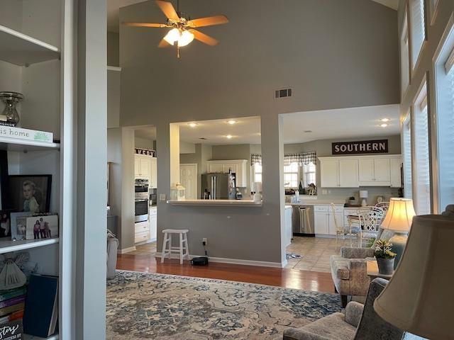 living room featuring ceiling fan, light hardwood / wood-style floors, and a towering ceiling