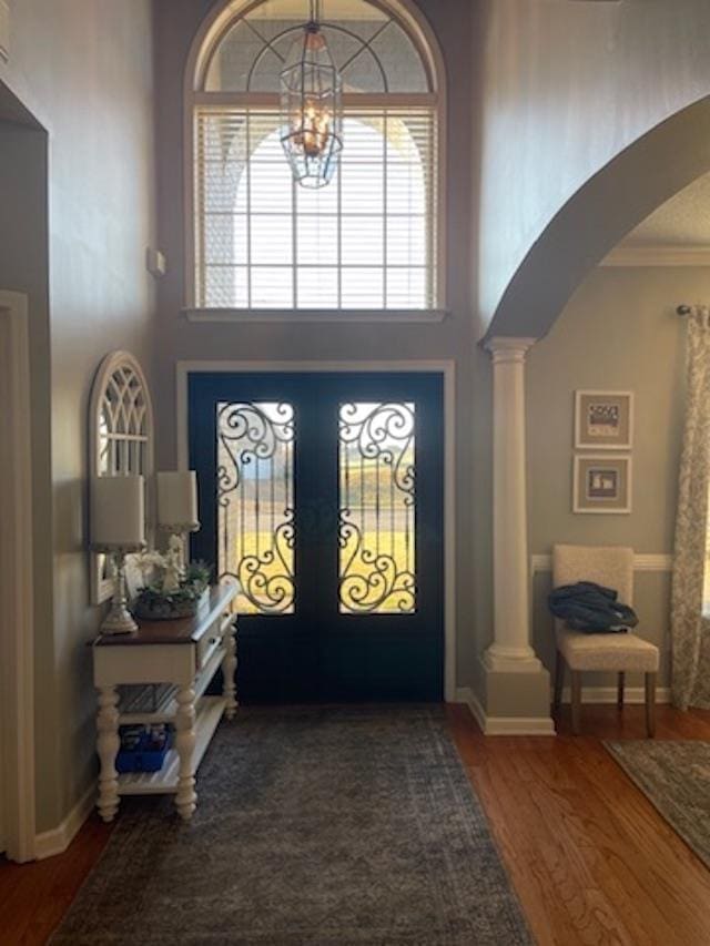 entryway featuring decorative columns, a notable chandelier, a high ceiling, and hardwood / wood-style flooring