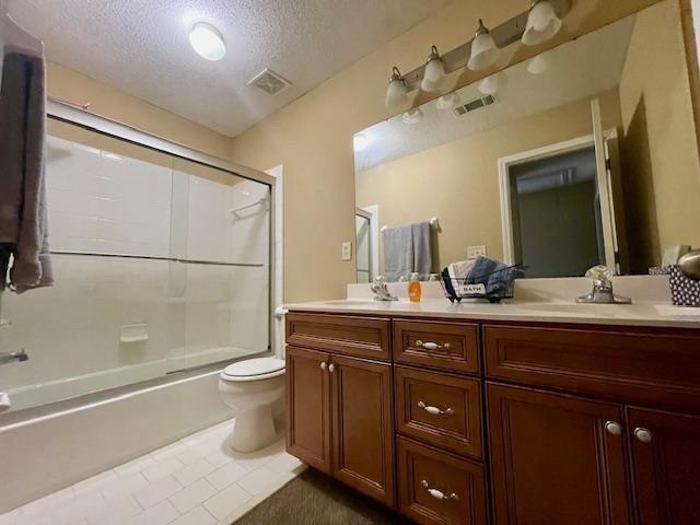 full bathroom with tile patterned floors, bath / shower combo with glass door, a textured ceiling, toilet, and vanity