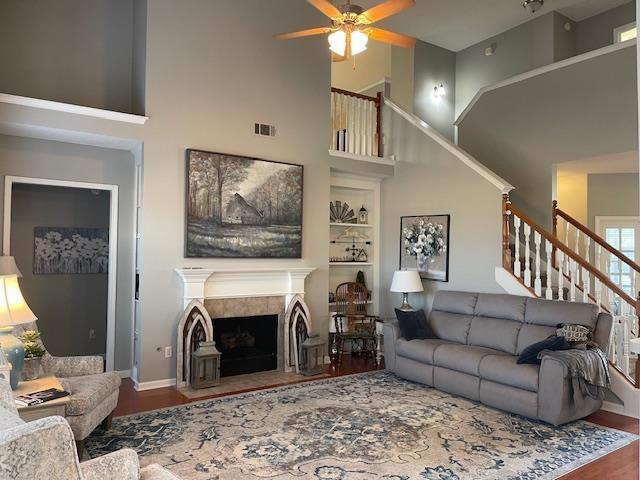 living room featuring hardwood / wood-style floors, ceiling fan, a towering ceiling, and a fireplace