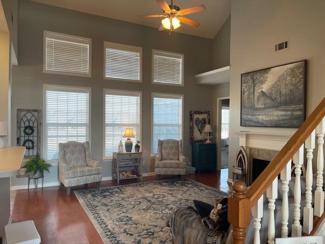 living room with a tiled fireplace, ceiling fan, dark wood-type flooring, and a high ceiling