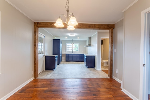 kitchen with blue cabinets, sink, hanging light fixtures, wall chimney exhaust hood, and wood-type flooring