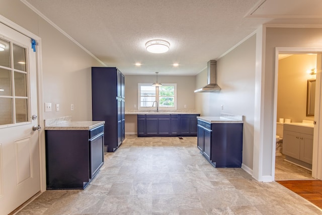 kitchen with blue cabinets, hanging light fixtures, wall chimney exhaust hood, ornamental molding, and a textured ceiling