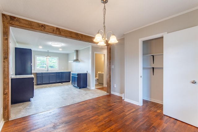 kitchen featuring blue cabinetry, decorative light fixtures, wood-type flooring, and wall chimney range hood