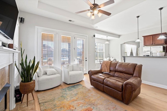 living room with light wood-type flooring, a raised ceiling, and ceiling fan