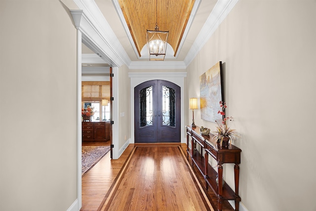 entryway featuring french doors, crown molding, a tray ceiling, a notable chandelier, and wood-type flooring