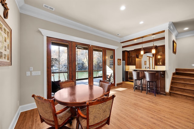 dining space with french doors, light wood-type flooring, and crown molding