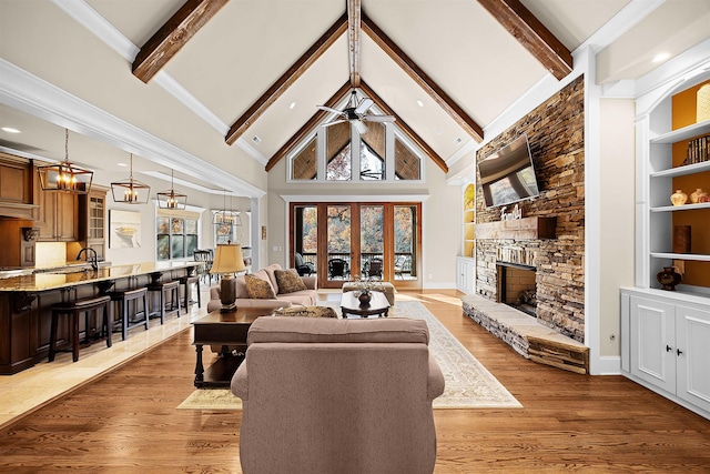 living room with beam ceiling, a stone fireplace, high vaulted ceiling, ceiling fan with notable chandelier, and hardwood / wood-style flooring