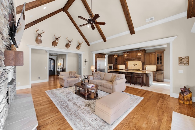 living room featuring beamed ceiling, light wood-type flooring, high vaulted ceiling, and ceiling fan