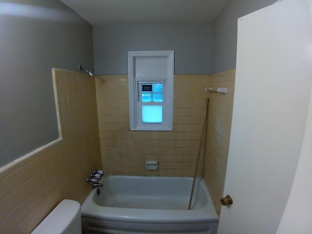 bathroom with tiled shower / bath combo, toilet, and tile walls