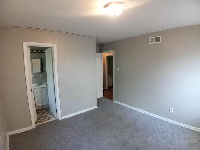 unfurnished bedroom featuring dark carpet, sink, and ensuite bath