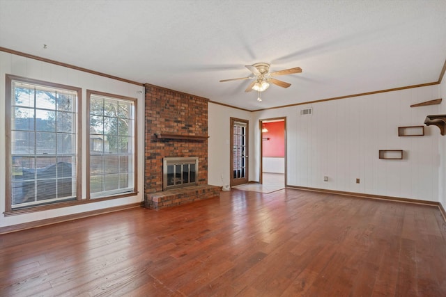 unfurnished living room with a brick fireplace, a textured ceiling, ceiling fan, crown molding, and wood-type flooring