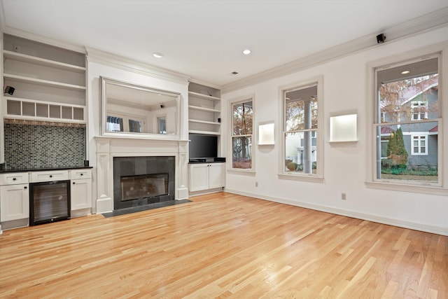 unfurnished living room featuring wine cooler, crown molding, and light hardwood / wood-style floors