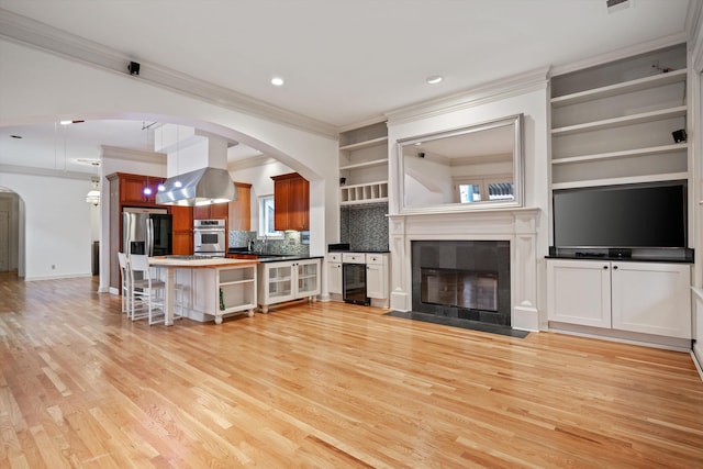 living room featuring sink, wine cooler, light hardwood / wood-style flooring, built in shelves, and ornamental molding