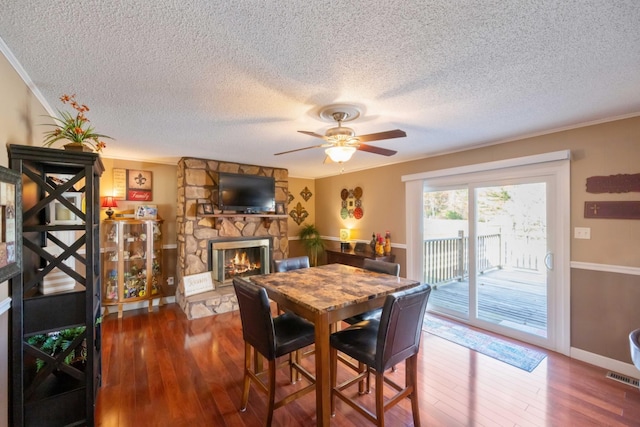 dining room featuring wood-type flooring, a textured ceiling, a stone fireplace, and ornamental molding