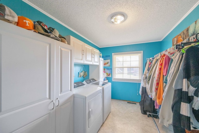 laundry area featuring cabinets, a textured ceiling, crown molding, and washing machine and clothes dryer