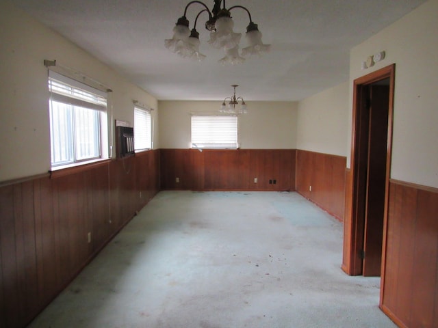 carpeted empty room featuring a chandelier and wooden walls