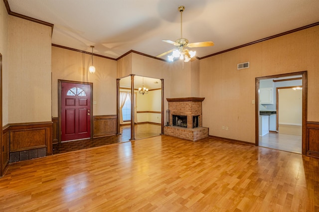 unfurnished living room featuring hardwood / wood-style floors, ceiling fan with notable chandelier, crown molding, and a brick fireplace