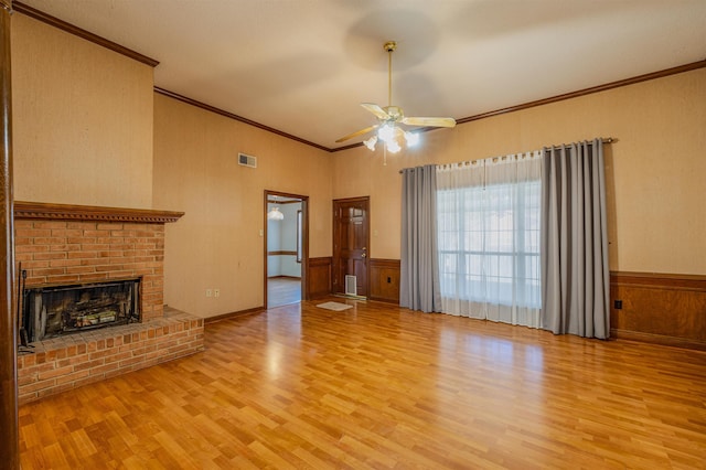 unfurnished living room featuring ceiling fan, light wood-type flooring, crown molding, and a brick fireplace