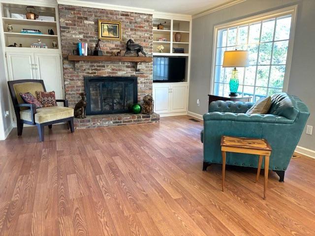 living room featuring a fireplace, wood-type flooring, built in shelves, and ornamental molding