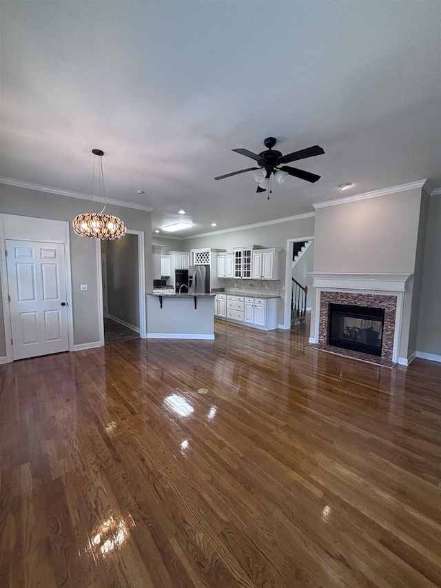 unfurnished living room featuring ornamental molding, ceiling fan with notable chandelier, and dark wood-type flooring