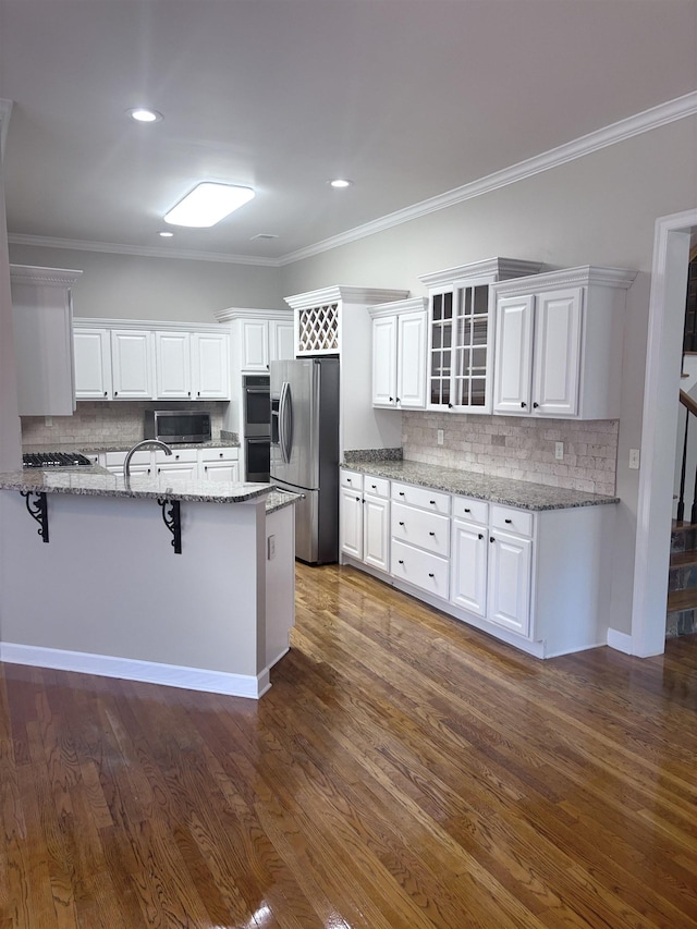 kitchen featuring white cabinetry, dark wood-type flooring, stainless steel appliances, light stone counters, and a breakfast bar area