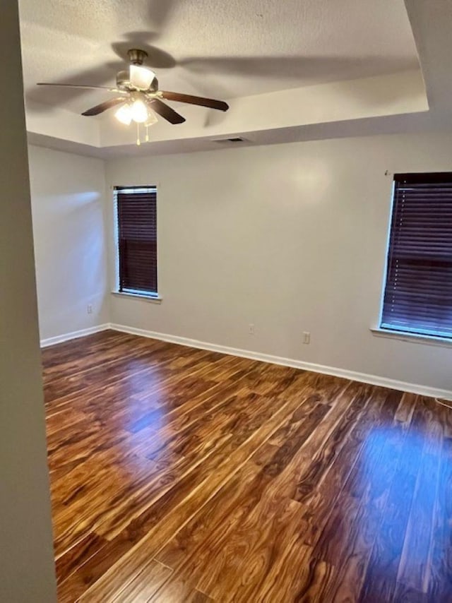 unfurnished room featuring a raised ceiling, ceiling fan, and dark wood-type flooring