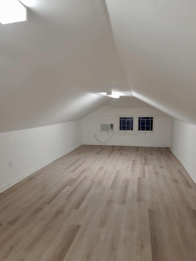 additional living space featuring lofted ceiling, a wall unit AC, and light hardwood / wood-style flooring