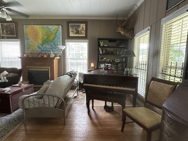 living area with wooden walls, ceiling fan, wood-type flooring, and a wealth of natural light