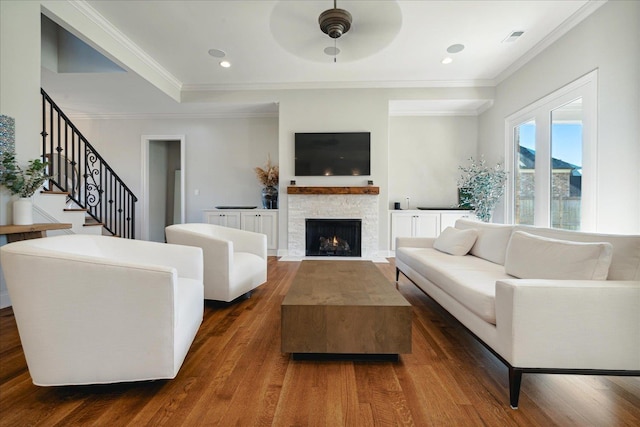 living room with dark hardwood / wood-style floors, ceiling fan, a stone fireplace, and ornamental molding