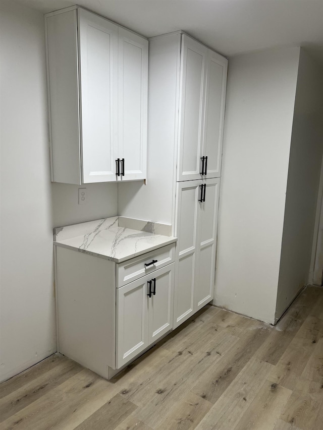 bar featuring light stone counters, light hardwood / wood-style flooring, and white cabinets