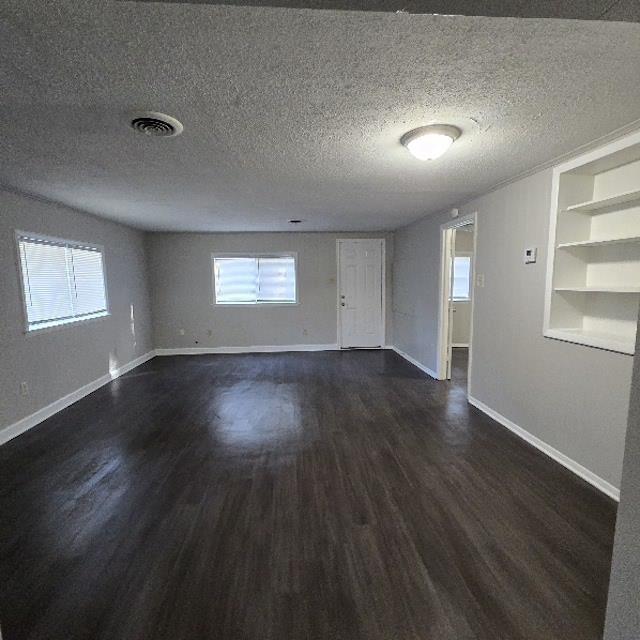 empty room with built in shelves, dark wood-type flooring, and a textured ceiling