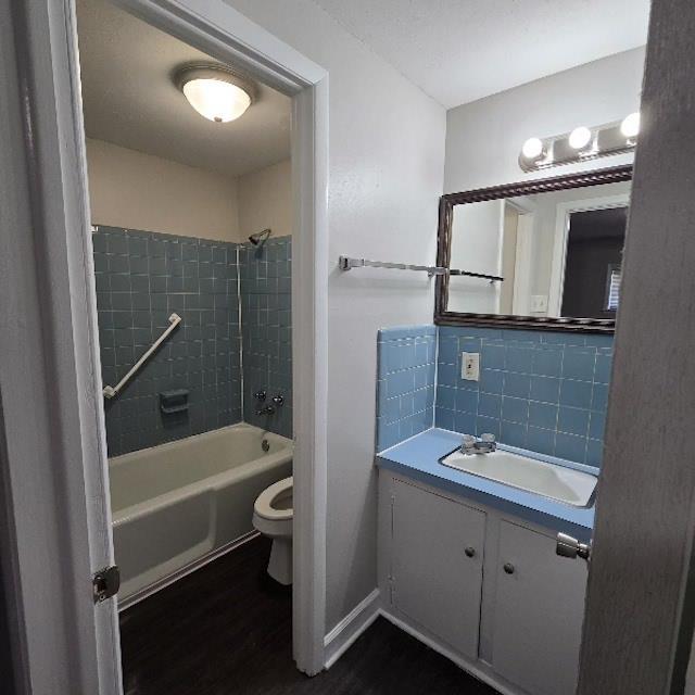 full bathroom featuring vanity, tiled shower / bath, hardwood / wood-style flooring, toilet, and tasteful backsplash